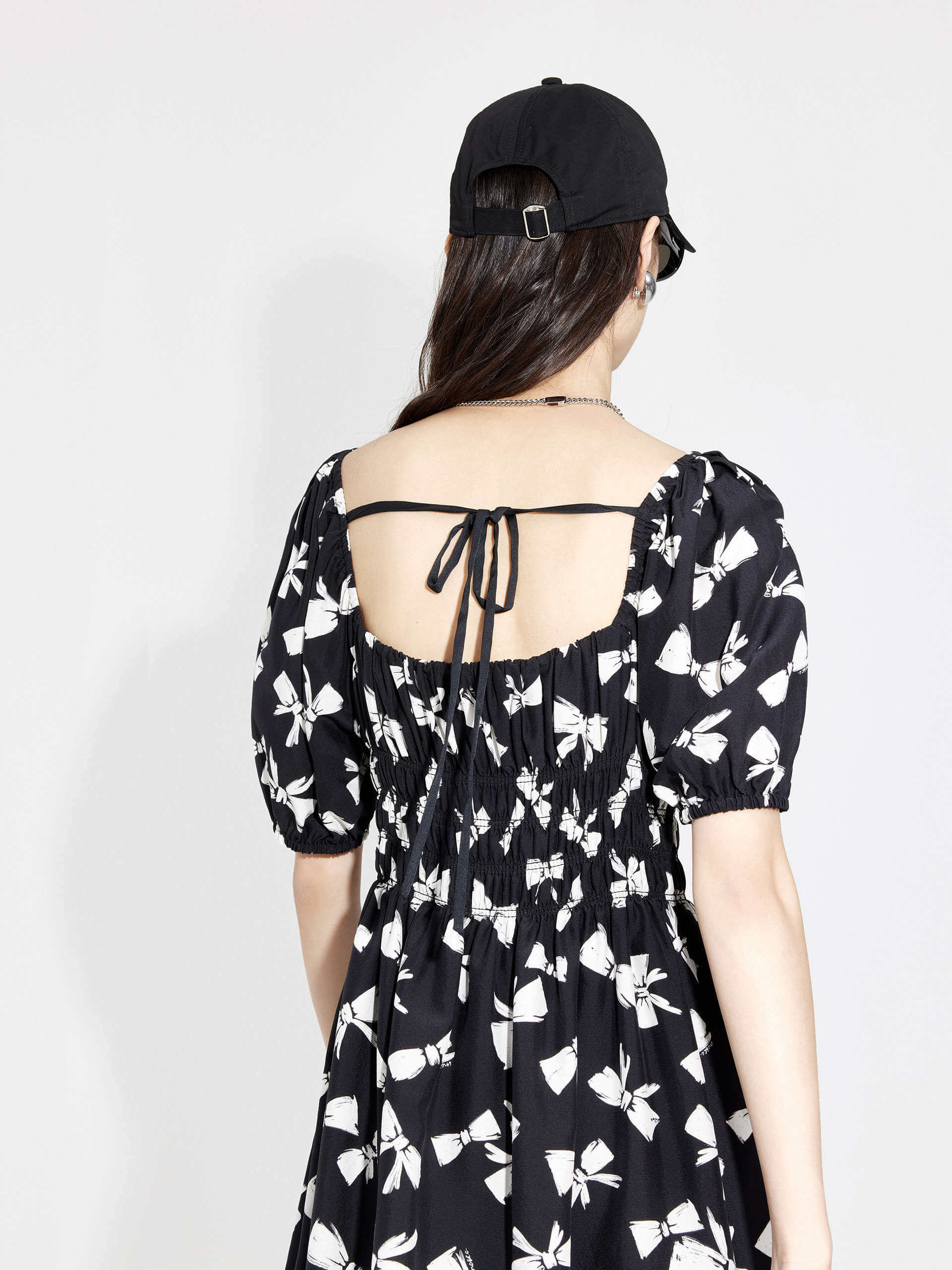 MO&Co. Women's Bowknot Pattern Flowy Midi Dress in Black. Crafted from luxurious silk and viscose blend fabric with an all-over bowknot print, self-tie details at back and square neckline, and elasticized shoulders for a smocked waist design.