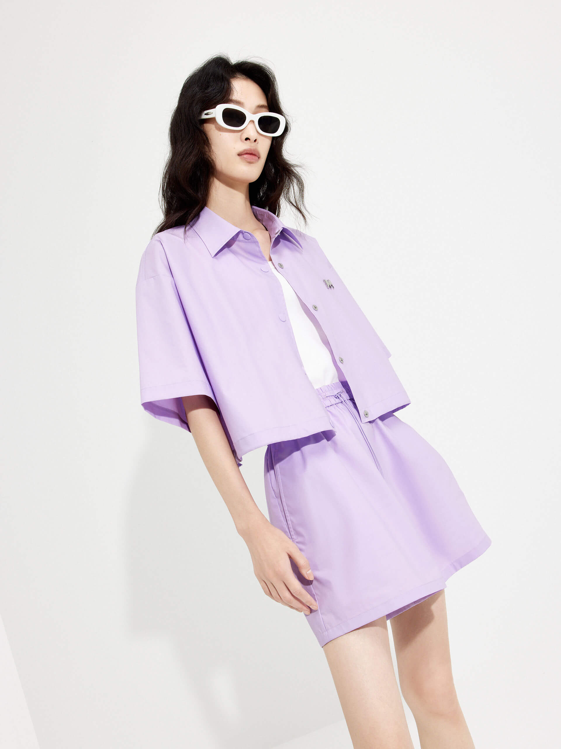 MO&Co. Women's Boxy Fit Cotton Shirt Jacket in Short Sleeves in purple features cropped, short sleeves, a button closure, and a M metallic embellishment at the front. Choose from color in purple and black, and pair with the matching shorts for a stylish look.