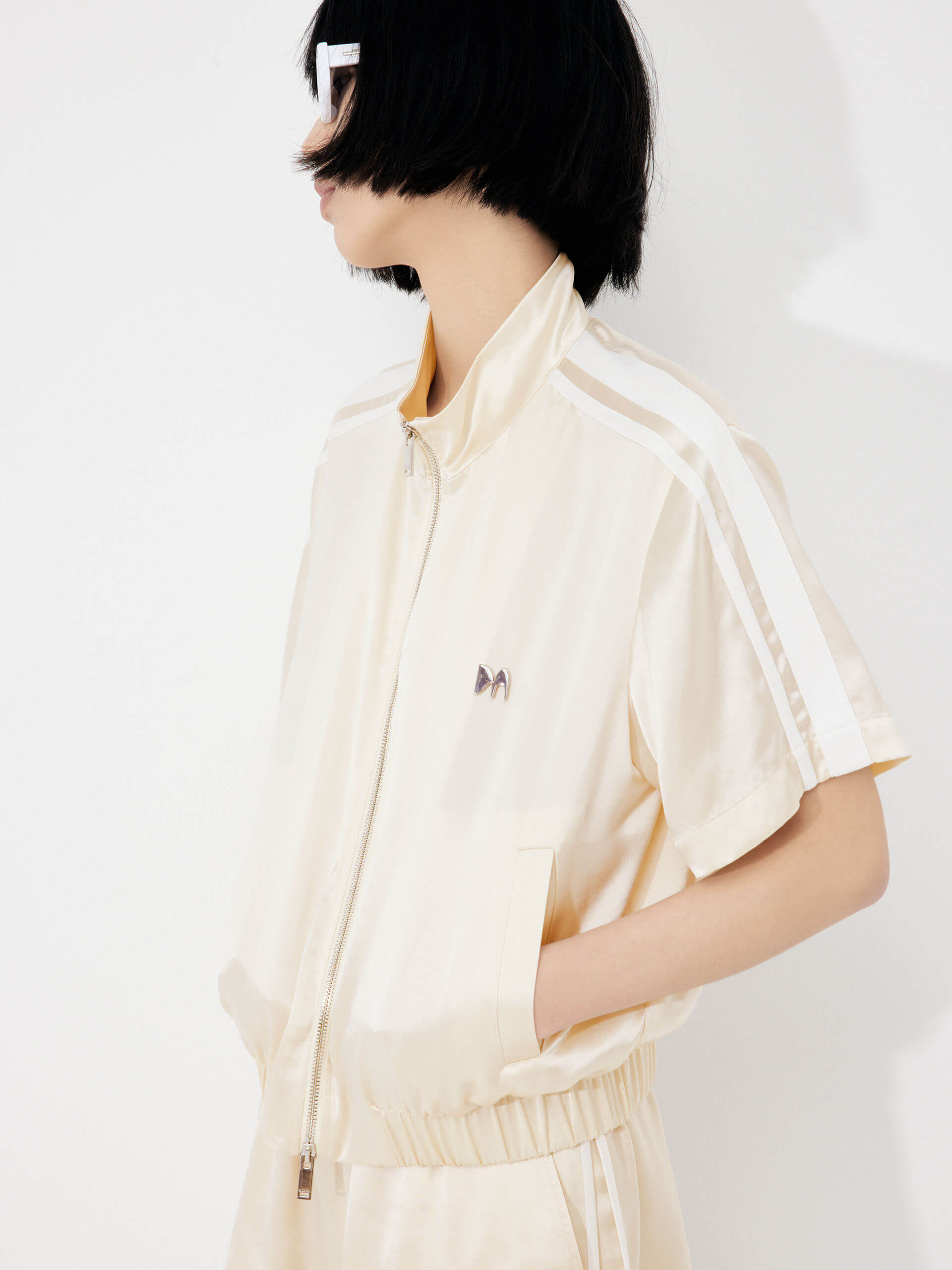 MO&Co. Women's Satin Acetate Blend Casual Track Jacket in Short Sleeves in Beige. Features: Loose fit, contrasting trim design, elasticized hem, side pockets & zip closure, and an acetate blend fabric for softness & comfort.