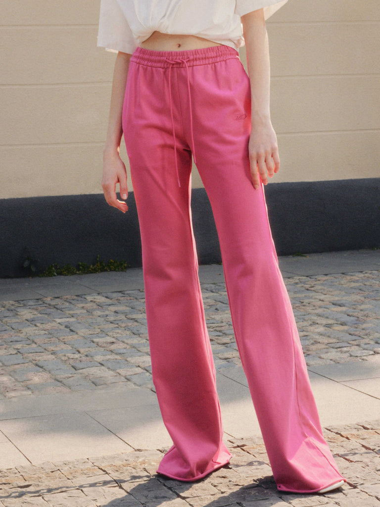 MO&Co.'s Drawstring Waist Causal Flared Sweatpants in Hot Pink. Crafted from soft cotton, these trousers feature a relaxed fit with drawstrings and elastic waistband for comfort. They also come with flared legs and double side pockets with MC embroidery details.