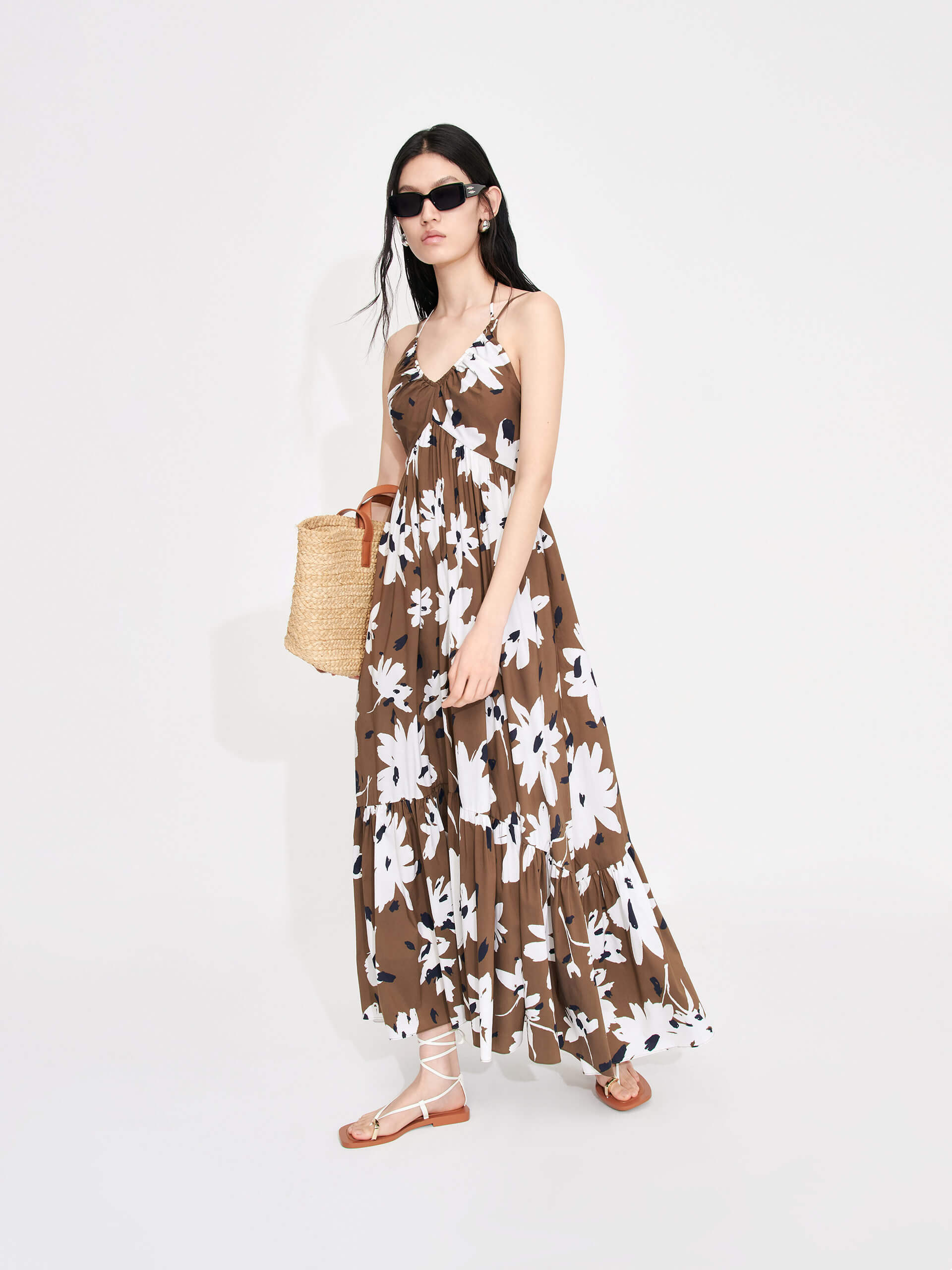 MO&Co. Women's Tropical Floral Print Vacation Maxi Dress in Brown features a V-neck, pleated details, cascading skirt and halterneck tie.