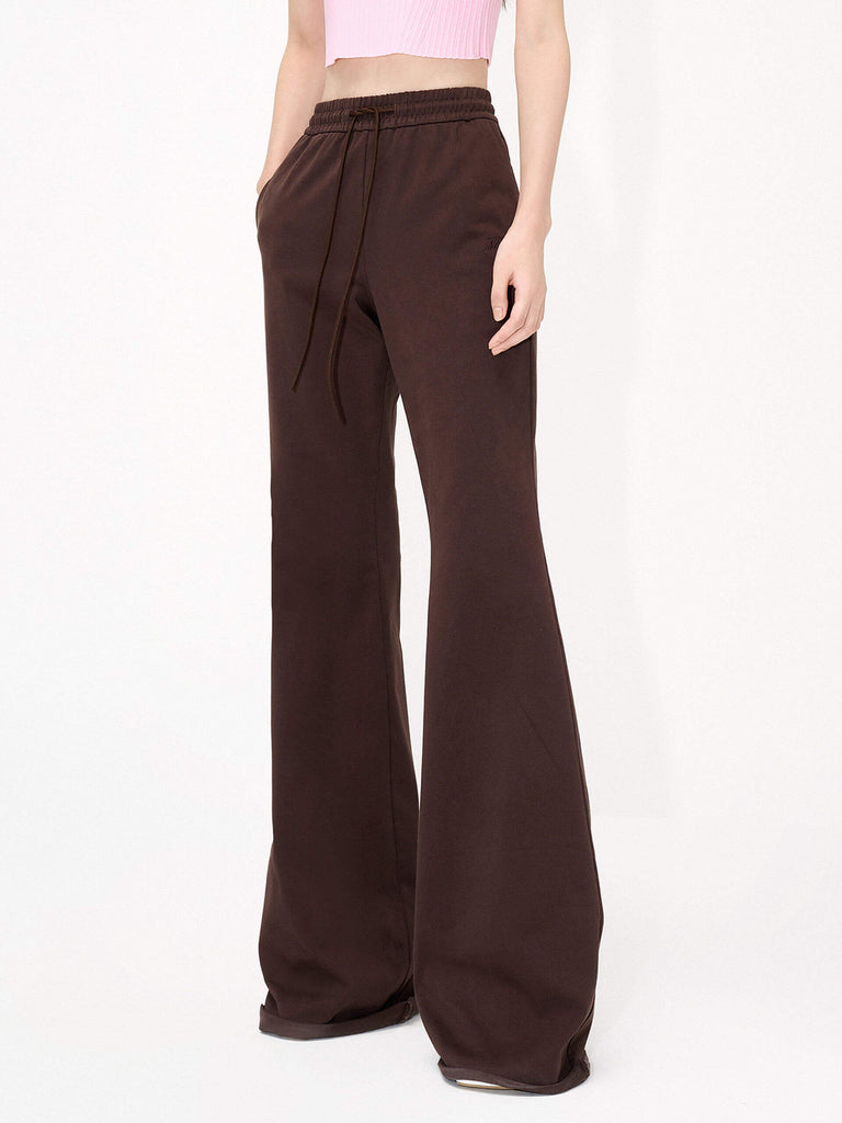 MO&Co.'s Drawstring Waist Causal Flared Sweatpants in Brown. Crafted from soft cotton, these trousers feature a relaxed fit with drawstrings and elastic waistband for comfort. They also come with flared legs and double side pockets with MC embroidery details.
