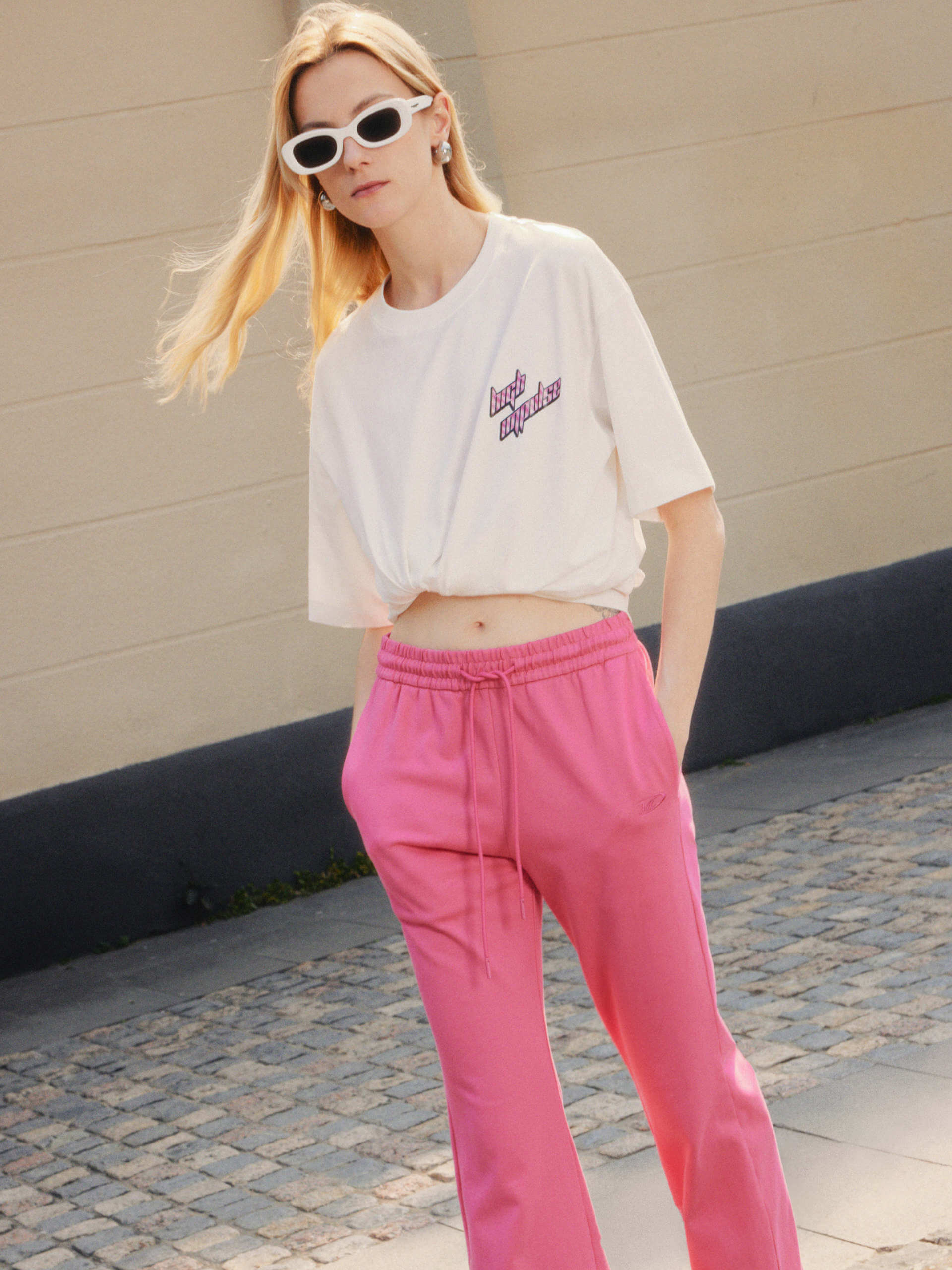 MO&Co.'s Drawstring Waist Causal Flared Sweatpants in Hot Pink. Crafted from soft cotton, these trousers feature a relaxed fit with drawstrings and elastic waistband for comfort. They also come with flared legs and double side pockets with MC embroidery details.