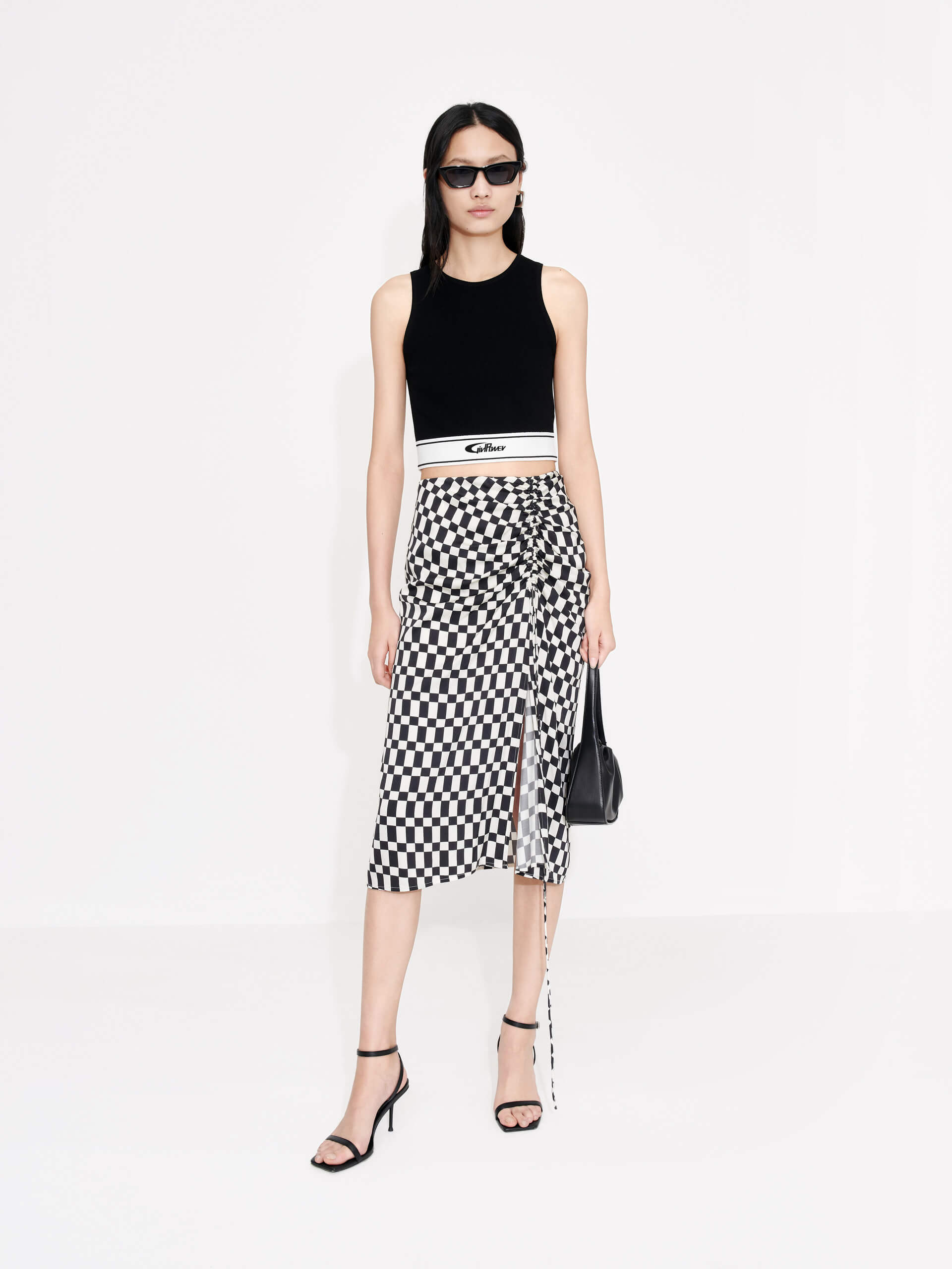 MO&Co. Women's Chessboard Pattern Skirt features modern bold chessboard pattern in black and white. Crafted with pleated drawstring design for an elegant look, finished with a hidden side zipper closure and side slit.