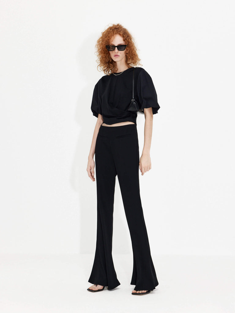 MO&Co. Women's Deconstructed Flared Pants in Black. Crafted from a lightweight, smooth acetate blend fabric, these pants feature a concealed side zipper, high waist with strap details and a seam detail along the front.