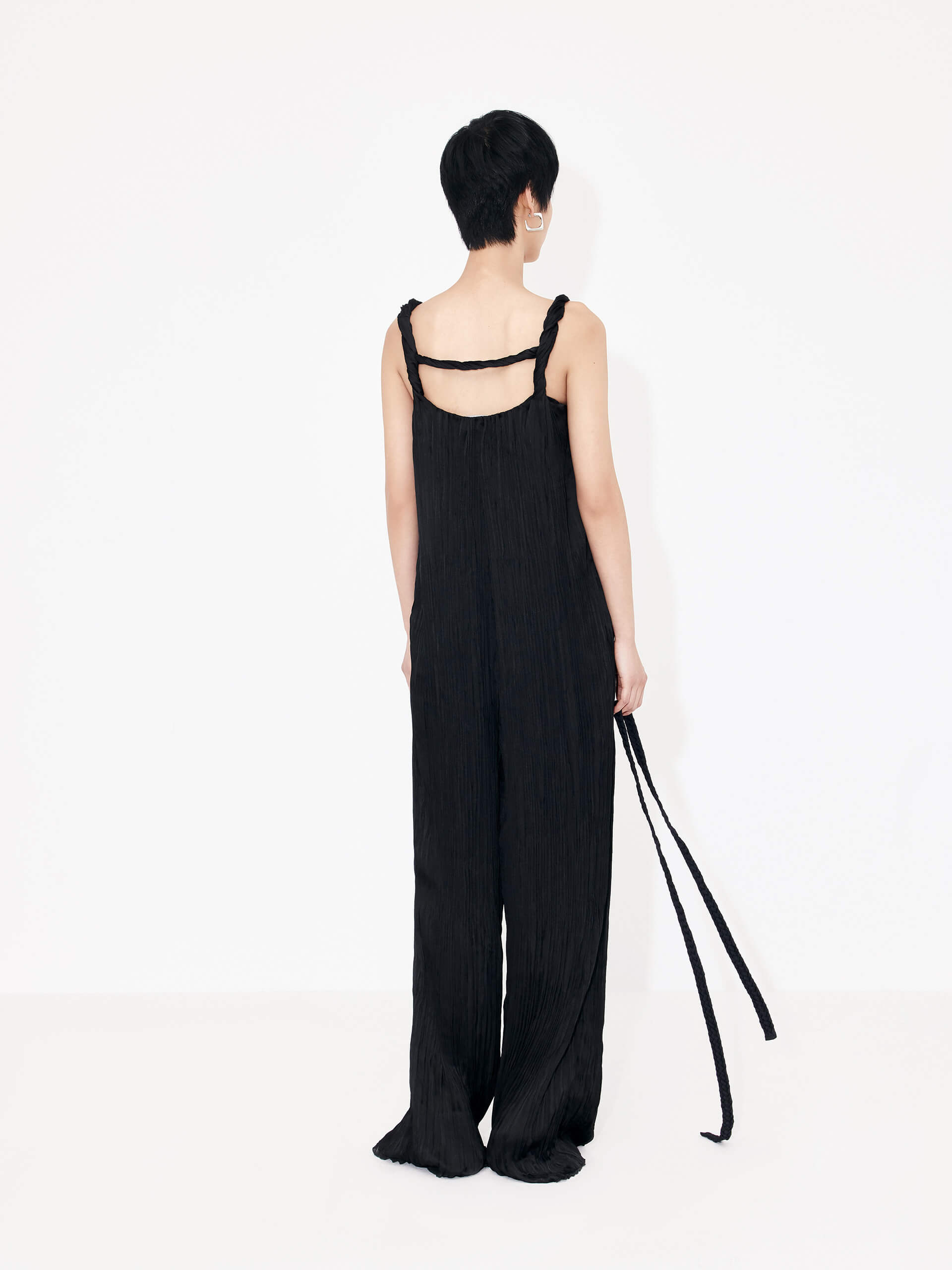 MO&Co. Women's Textured Wide Leg Jumpsuit in Black features an included belt & double side pocket design. Its elegantly draped & twisted shoulder strap completes the look for a timeless classic.