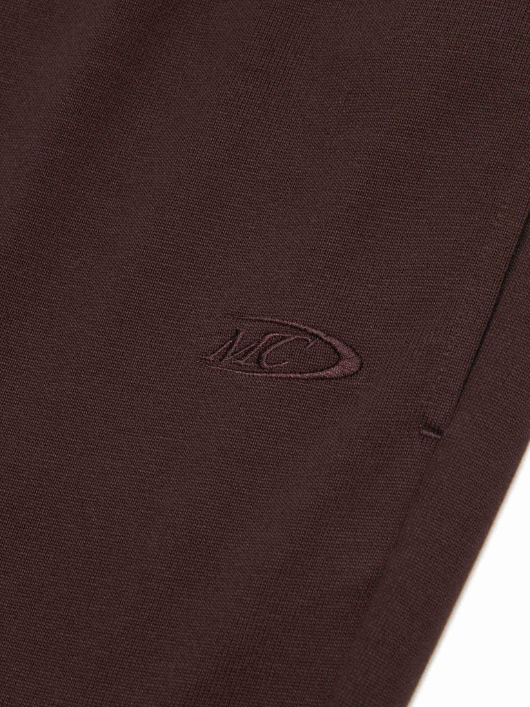MO&Co.'s Drawstring Waist Causal Flared Sweatpants in Brown. Crafted from soft cotton, these trousers feature a relaxed fit with drawstrings and elastic waistband for comfort. They also come with flared legs and double side pockets with MC embroidery details.