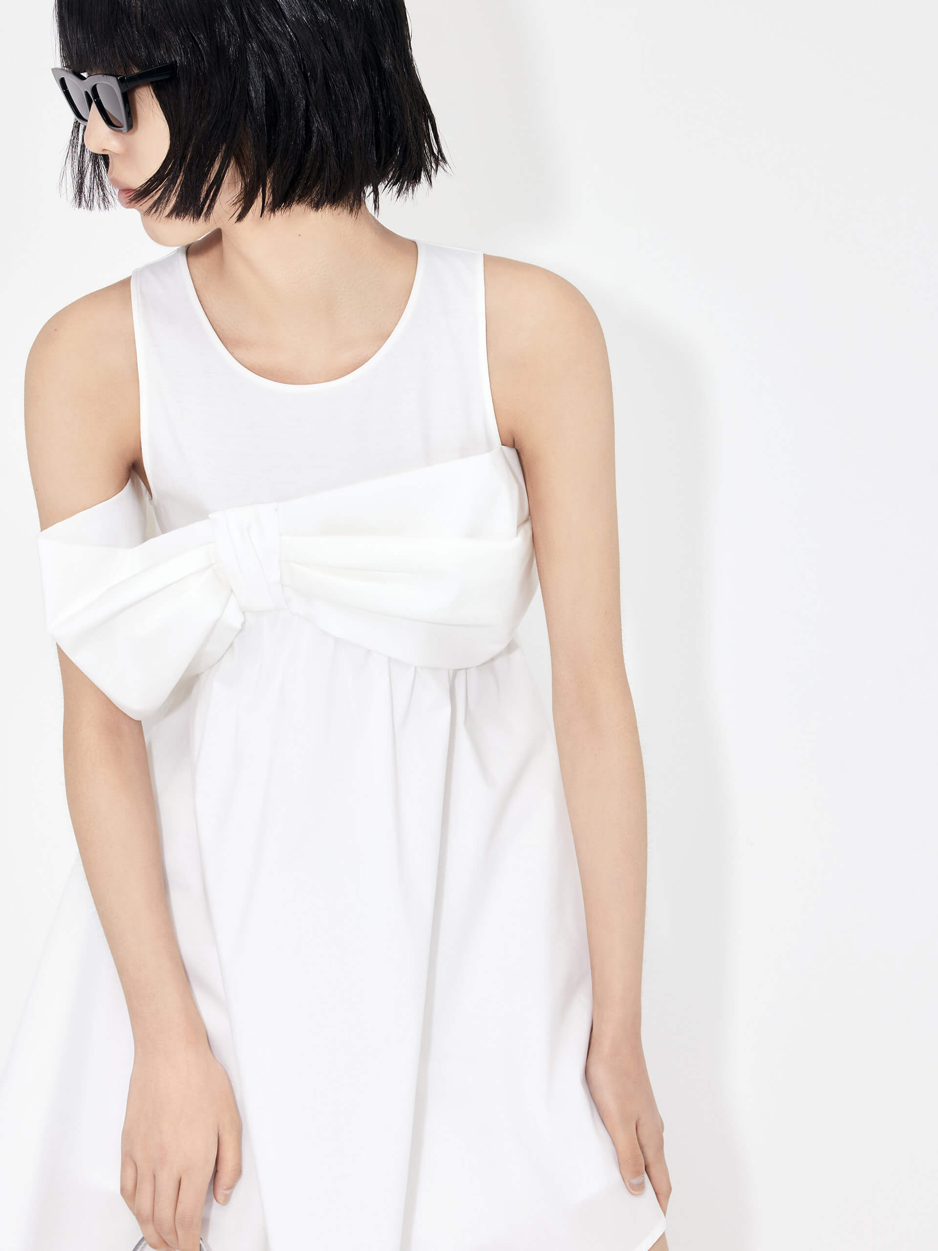 MO&Co. Bowknot Front Mini Dress in White with sleeveless design. Crafted from a soft and breathable cotton blend, this feminine and sophisticated piece features an a-line silhouette with bowknot front details for an eye-catching look.