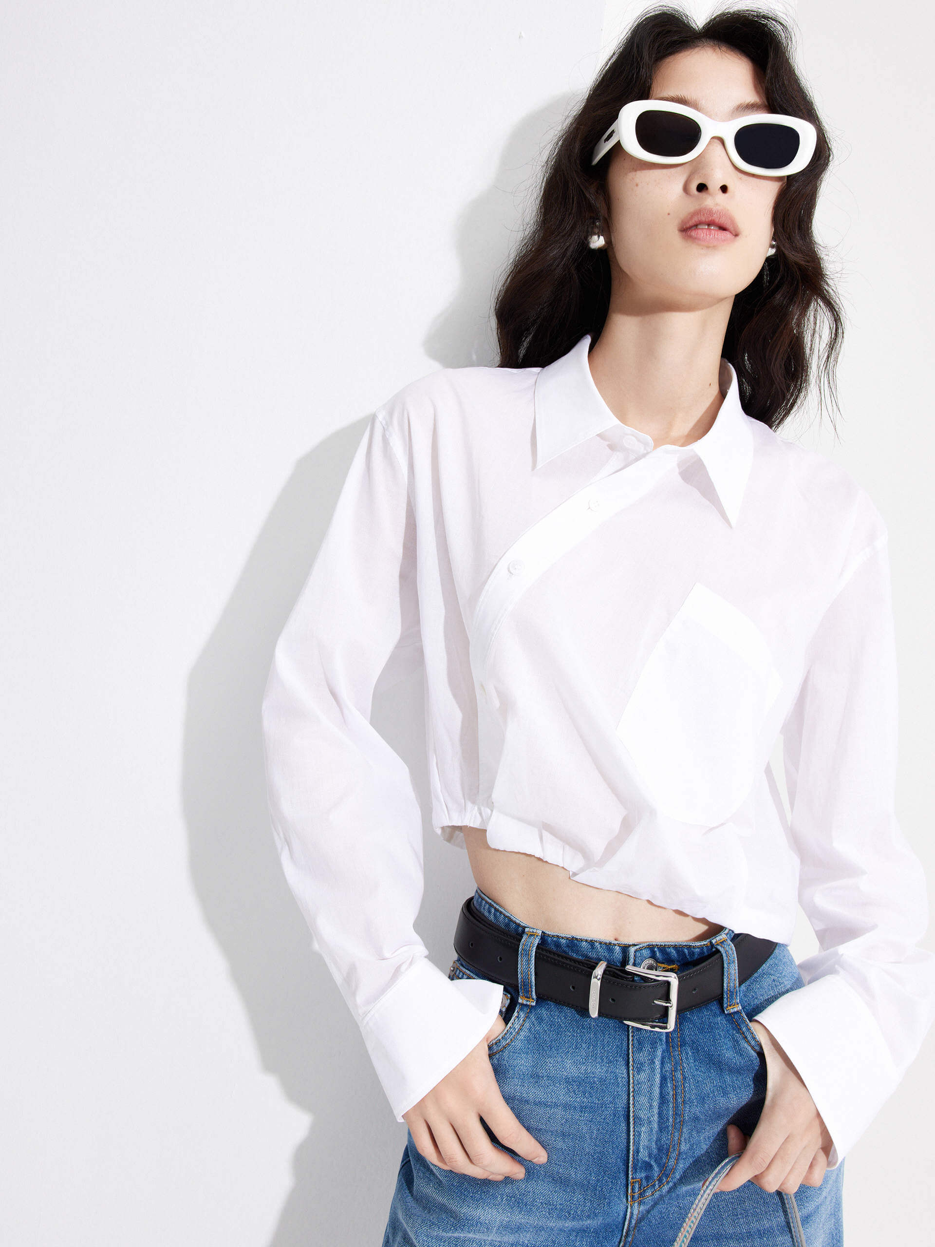 MO&Co. Women's Slanted Placket Cropped Shirt in White. Crafted with a stylish cropped silhouette and slanted placket design, this fashion-forward piece is bound to turn heads. Plus, it's complete with a front pocket and elastic hem for a unique look.