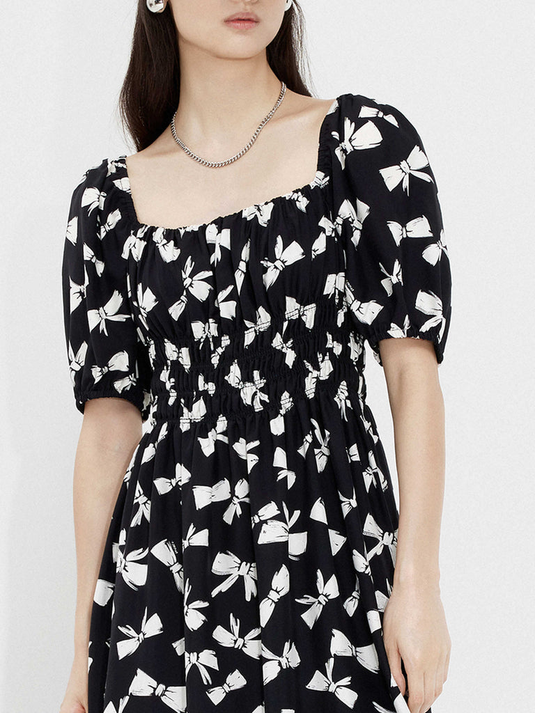 MO&Co. Women's Bowknot Pattern Flowy Midi Dress in Black. Crafted from luxurious silk and viscose blend fabric with an all-over bowknot print, self-tie details at back and square neckline, and elasticized shoulders for a smocked waist design.