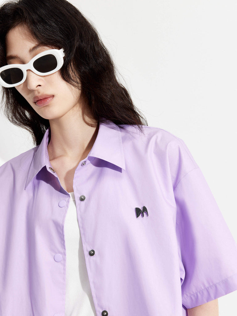 MO&Co. Women's Boxy Fit Cotton Shirt Jacket in Short Sleeves in purple features cropped, short sleeves, a button closure, and a M metallic embellishment at the front. Choose from color in purple and black, and pair with the matching shorts for a stylish look.